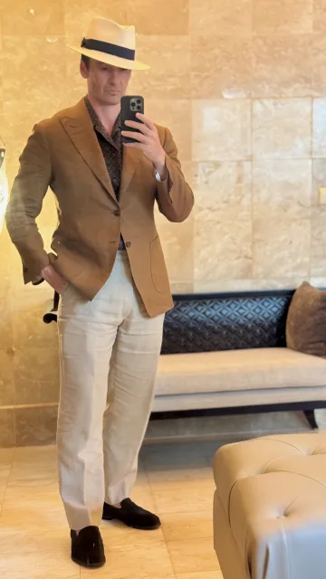 John Philip Green in a brown blazer, cream trousers and a straw hat.
