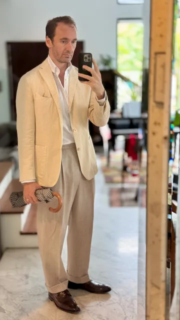 John Philip Green in a cream jacket and pale pleated trousers.
