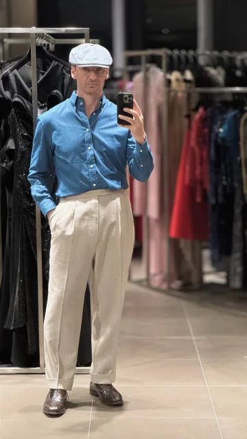 John Philip Green in a blue shirt, cream pleated trousers and flat cap.