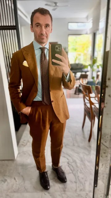 John Philip Green in a brown suit with a blue shirt and striped tie.