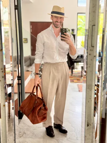 John Philip Green in a pale pink shirt, cream trousers and straw hat, carrying a brown bag.