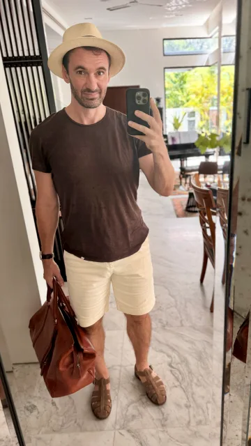 John Philip Green in a brown T-shirt, pale shorts and straw hat.