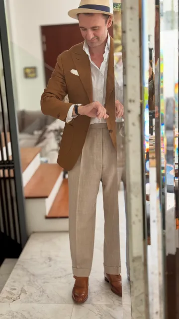 John Philip Green in a brown blazer, pink shirt, patterned tie, pale trousers and straw hat.