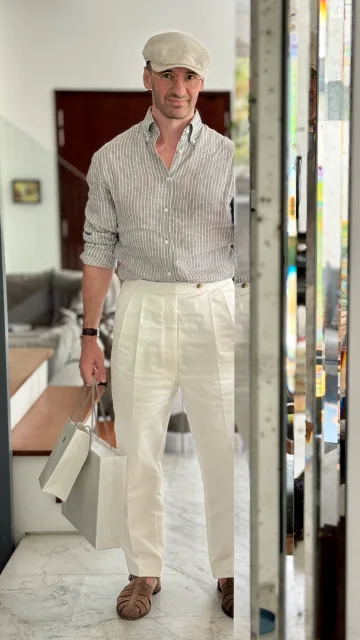 John Philip Green in a checked shirt, cream trousers and flat cap, carrying a pale tote.