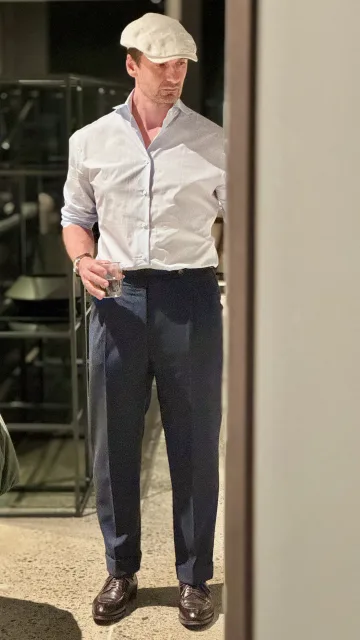 John Philip Green in a pale shirt, dark pleated trousers and flat cap.