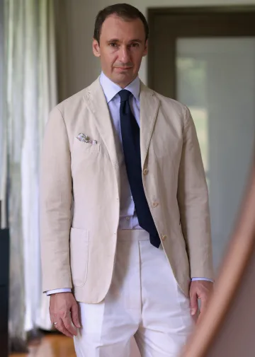 John Philip Green in a pale suit, striped shirt and dark tie.
