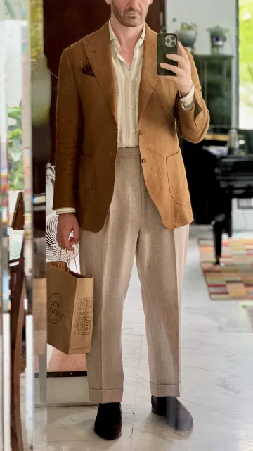 John Philip Green in a brown blazer and pale trousers with an open-collar shirt.