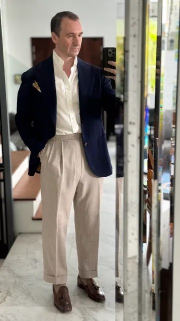 John Philip Green in a navy blazer, white shirt and cream pleated trousers.