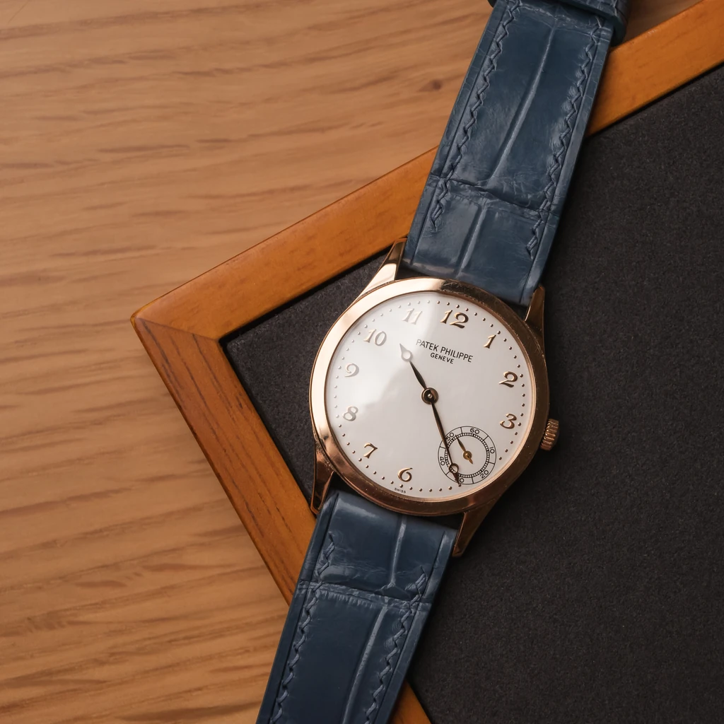 Patek Philippe Calatrava with a blue strap crossing a black inset in a wooden surface