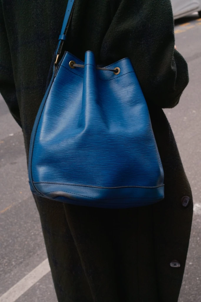 A blue Epi leather Noé worn against a dark coat; the drawstring gathers the opening